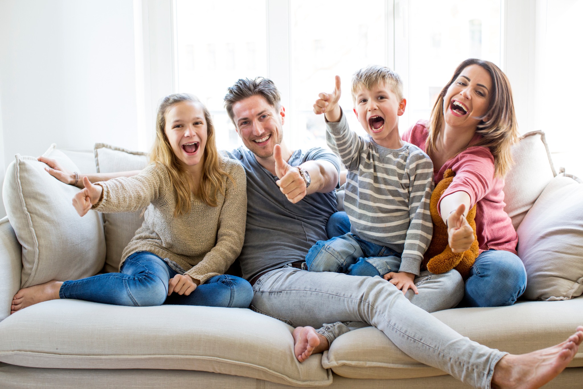 Familie sitzt gemeinsam auf einem Sofa und zeigt den Daumen nach oben